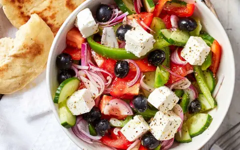 Frischer griechischer Salat mit Tomaten, Gurken, roten Zwiebeln, Oliven und Feta-Käse, serviert mit Fladenbrot.