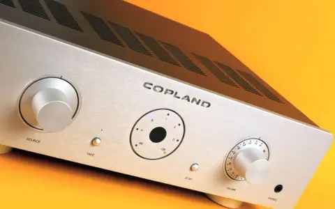 Srebrny wzmacniacz Copland CSA 100 z pokrętłami Source i Volume, przyciskiem Tape oraz wskaźnikami.