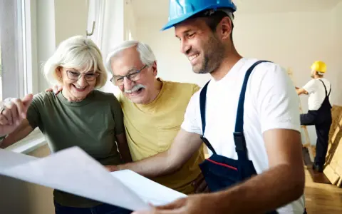 Pareja mayor sonríe mientras revisa planos con un constructor. Posibles bonificaciones mayores 65 años para su proyecto.
