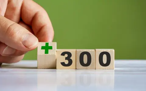 Dłoń układa kostkę z zielonym plusem obok kostek z napisem "300". To dobry start dla kogoś, kto chce zacząć coś nowego.