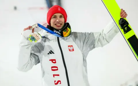 Kacper Tomasiak, skoczek narciarski, z dumą prezentuje medal i narty.