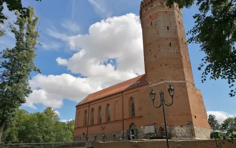 Zamek Człuchów, ceglana wieża i budynek muzeum pod błękitnym niebem z chmurami.