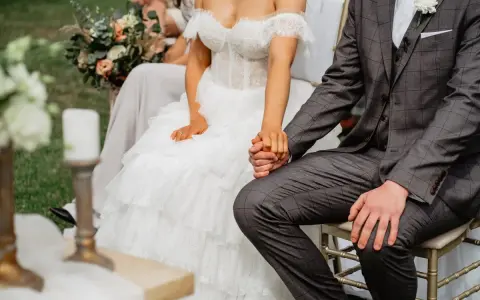 Para spowiedzi przedślubnej lub formalności w USC: panna młoda w koronkowej sukni i pan młody w garniturze trzymają się za ręce.