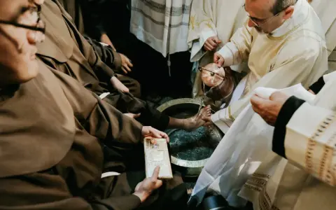 During a holy Thursday Catholic homily, a priest washes the feet of a man in a basin, symbolizing Christ's humility.