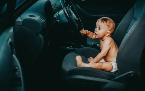 Maluch w pieluszce siedzi za kierownicą, jakby zastanawiał się, od kiedy dziecko może jeździć z przodu.