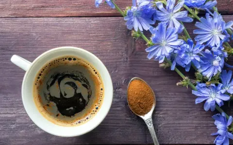Taza de café de achicoria, con flores azules y una cucharada de polvo de achicoria, ideal para aprender como preparar achicoria en cafetera.