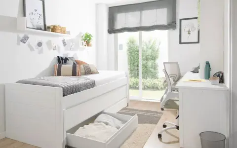 Habitación estrecha y alargada con cama blanca, escritorio y silla. Ventana grande con vistas al jardín.