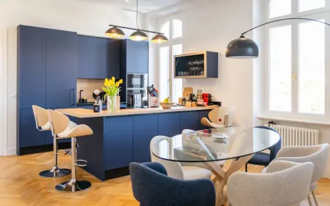 Élégante petite cuisine ouverte avec îlot central bleu marine, tabourets en bois et table en verre.