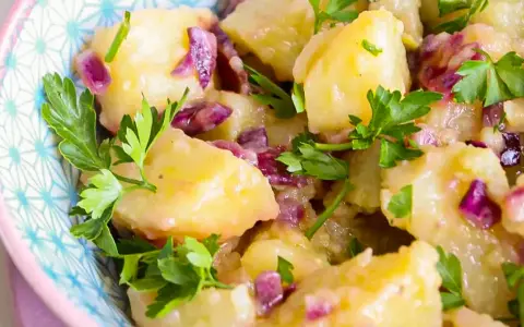 Salade de pomme de terre crémeuse avec des oignons rouges et du persil frais, servie dans un bol décoratif.