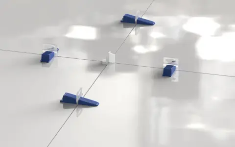 Sistema de nivelación de baldosas con cuñas azules y separadores blancos. La **matajunta desplazada** asegura una instalación perfecta.