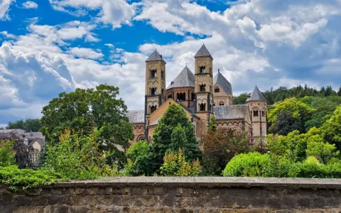 A grand Romanesque abbey, where Benedictine monks lived, stands amidst lush greenery under a dramatic sky.