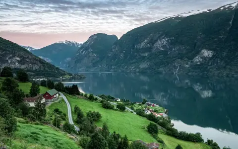 Grönskande bergssluttningar med hus vid en fjord i Norge. Perfekt för att planera dina inreseregler Norge.