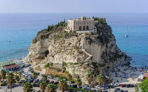 Santuario di Santa Maria dell'Isola a Tropea, regione Calabria, su uno sperone roccioso a picco sul mare azzurro, con spiaggia e palme.