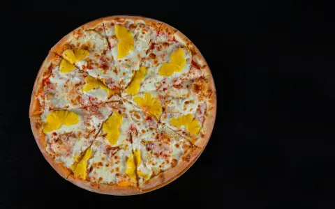 Pizza hawajska z kurczakiem i ananasem na czarnym tle.