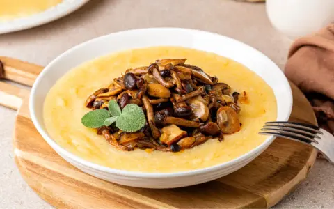 Polenta cremosa con champiñones salteados y una ramita de salvia. Un plato reconfortante que te hará preguntar: ¿polenta que es? ¡Deliciosa!
