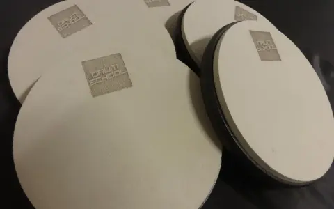 Kilka okrągłych, beżowych padów perkusyjnych z logo "DRUM SCHOOL" leży na czarnym tle.