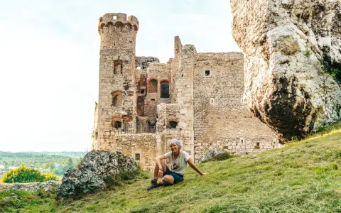 Kobieta odpoczywa na trawie przed ruinami zamku na Szlaku Orlich Gniazd. Ile zamków czeka na odkrycie?