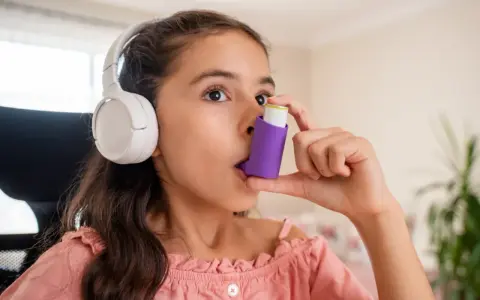 Mädchen mit Kopfhörern benutzt Inhalator gegen Asthma durch Stress.