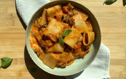 Piatto di pasta alla siciliana con rigatoni, melanzane e pomodoro, guarnito con basilico fresco.
