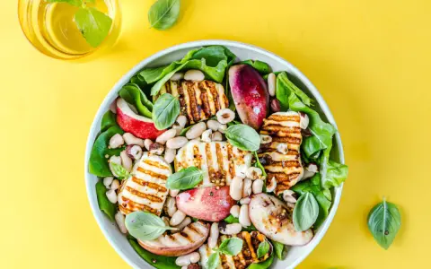 Pyszna sałatka z grillowanym halloumi, fasolką, jabłkiem i orzechami, udekorowana listkami bazylii.
