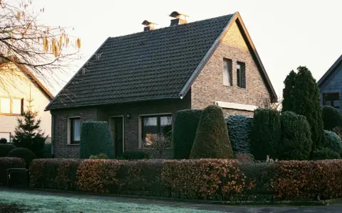 Ein gepflegtes Einfamilienhaus mit Ziegelfassade und dunklem Dach. Die Frage "wie viel kostet ein haus" wird durch die idyllische Szenerie aufgeworfen.