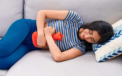 Joven con bolsa de agua caliente en el abdomen, aliviando el dolor de cólicos.