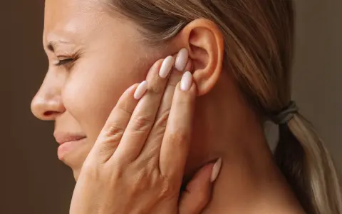 Une femme se tient l'oreille, le visage crispé, comme si elle entendait un bruit sourd dans les oreilles.