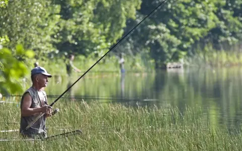 Mężczyzna łowi ryby w trzcinach nad jeziorem. Idealny dzień, kiedy sezon na szczupaka w pełni.