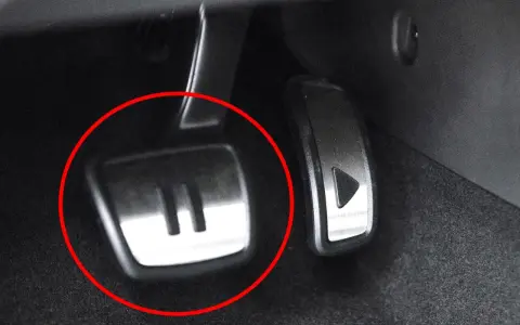 Metalowe pedały w samochodzie, jeden z symbolem "II" (auto hold) i drugi z trójkątem.