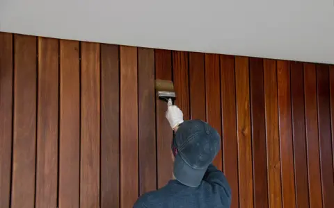 Application d'une finition sur un lambris en bois. Le résultat avant/après est saisissant, révélant la beauté naturelle du bois.