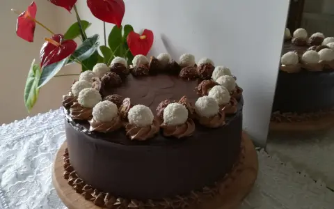 Czekoladowy tort udekorowany pralinami Lindt i Ferrero Rocher, obok czerwone anturium.