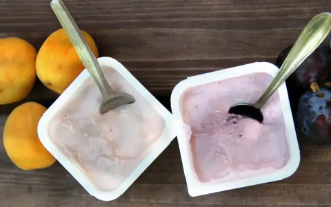 Dwa kubeczki jogurtu z owocami i łyżeczkami na drewnianym tle.