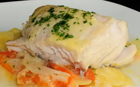 Cogote de merluza jugoso y tierno, servido sobre patatas y tomate, con un toque de perejil fresco.