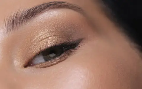 Maquillage paupière tombante : ombre dorée scintillante, trait d'eye-liner fin et cils longs pour un regard sublimé.