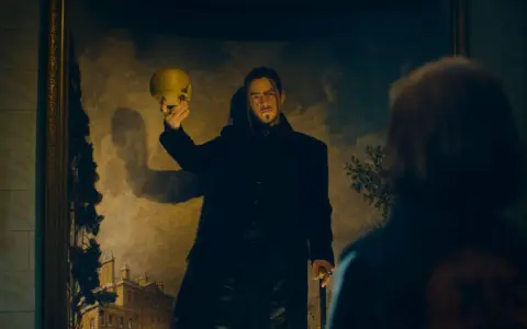 En man i svart rock håller upp en gul skalle framför en målning. Kanske en scen från skurkarnas skurk film.