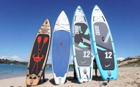 Vier Stand Up Paddles am Strand. Die Boards zeigen verschiedene Designs und Größen, die die Vor- und Nachteile von Stand up paddling beeinflussen können.