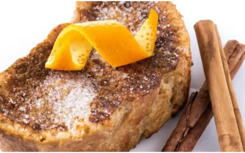 Torrijas al horno espolvoreadas con azúcar y canela, decoradas con piel de naranja y acompañadas de ramas de canela.