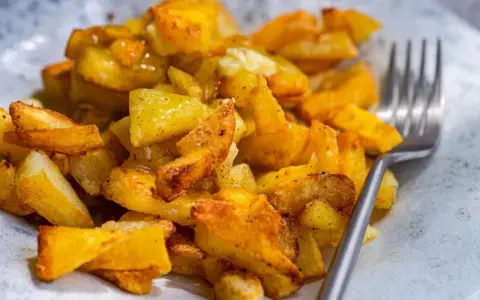 Un plato de patatas asadas doradas y crujientes, sazonadas con hierbas y especias, listas para ser disfrutadas con un tenedor.