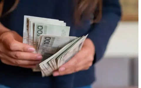 Dłonie trzymające plik polskich banknotów 100 zł. Zastanawiasz się, urlop wychowawczy ile płatny?