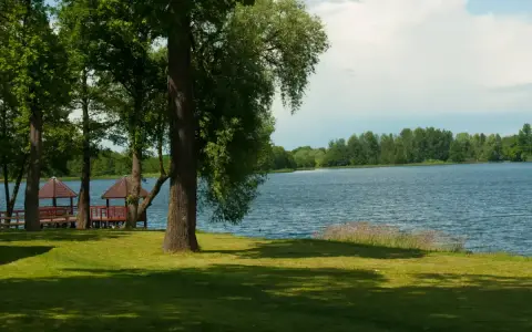 Malownicze jezioro Grabowo z altanami na pomoście, otoczone zielenią i drzewami.