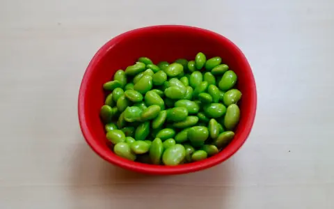 Czerwona miseczka pełna zielonych ziaren soi. Czy to edamame? Tak, to właśnie edamame, zdrowe i pyszne!