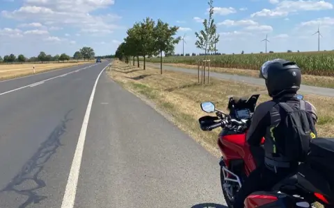 Motociclista su strada panoramica Foresta Nera, con campi di mais e pale eoliche all'orizzonte.