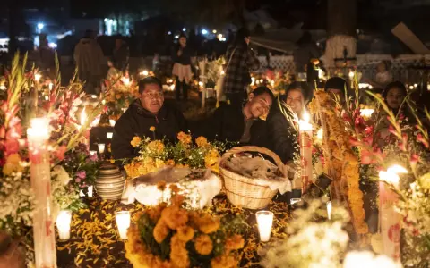 Rodzina przy grobie ozdobionym świecami i kwiatami na Dia de los Muertos.