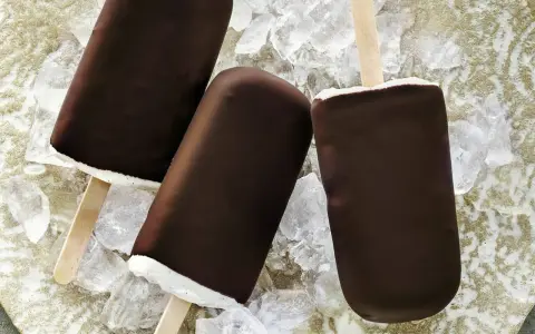 Drei Schokoladen-Vanilleeis am Stiel liegen auf Eiswürfeln.