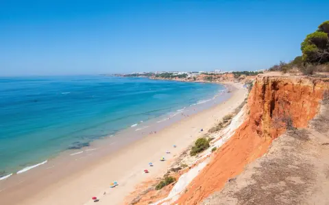 Blick auf den Strand Praia da Falésia mit seinen roten Felsen und der Stadt im Hintergrund.
