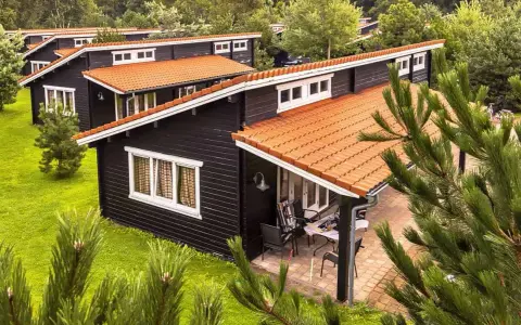 Czarny bungalow z pomarańczowym dachem, otoczony zielenią. To idealne miejsce na wypoczynek, co to znaczy bungalow?