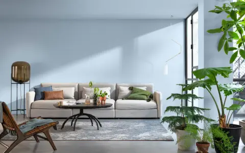 Jasny salon z wygodną kanapą, stolikiem kawowym i dużą ilością roślin. Sufit w kolorze ścian tworzy spójną, spokojną atmosferę.