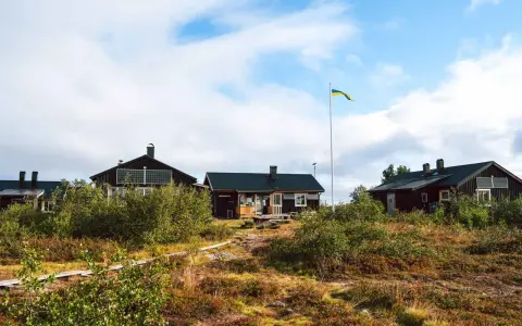 Mörka trähus med solpaneler och en svensk flagga som vajar. Ett charmigt vandrarhem i Dalarna, omgivet av vildmark.