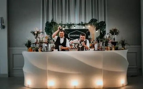 Dwóch barmanów przygotowuje drinki przy nowoczesnym, podświetlanym barze. To idealny drink bar na wesele, oferujący orzeźwiające napoje.
