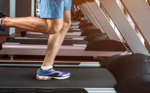 Gambe muscolose in movimento su un tapis roulant, simbolo di corsa indoor e allenamento.